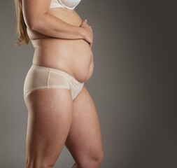 A woman with a large belly is wearing a bra and panties. Concept of confidence and self-assurance, as the woman stands tall and proud despite her weight. Gray background
