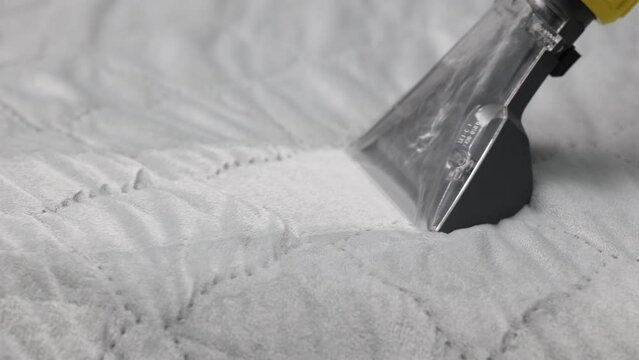 Professional cleaning of the mattress with a washing vacuum cleaner from debris and hair, close-up. A small nozzle of the mopping vacuum cleaner is used to remove the dirt of the mattress