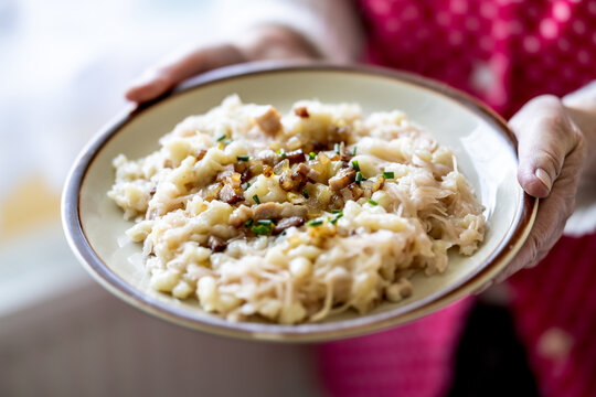 The hands of a senior home cook hold a plate with a national Slovak dish: Strapacky - Bryndzove Halusky