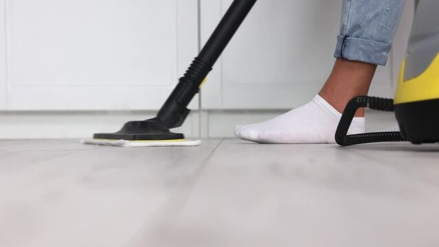 Female housewife with white socks removing germs by hot steam od pressure from white floor indoors. Close up of legs of man washing parquet laminate with steam mop