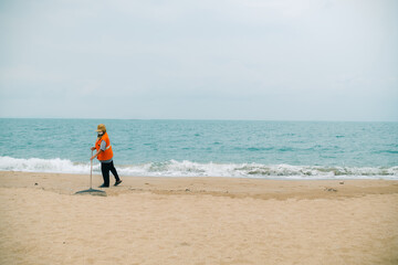 A cleaner in an orange uniform are cleaning up trash on the beach