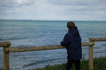 Adolescent en bord de mer  qui regarde vers l'océan, l'horizon.