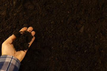 View from above. Copy space. Hand with a handful of earth over brown fertile soil. A farmer holds a...