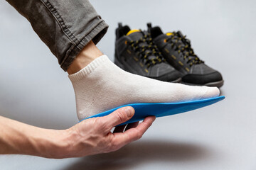 Close up of man hands fitting orthopedic insoles on a gray background.