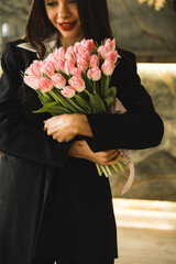 A pretty woman in a black suit holds fresh tulips flowers.Tulips in the hands of a woman.Business lady rejoices at the flowers.Spring concept