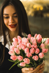 A pretty woman in a black suit holds fresh tulips flowers.Tulips in the hands of a woman.Business lady rejoices at the flowers.Spring concept
