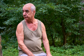 Naklejka na ściany i meble Pensive elderly man pensioner in a T shirt in a forest on a picnic
