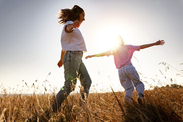 Two happy playful young girls runs in sunset field