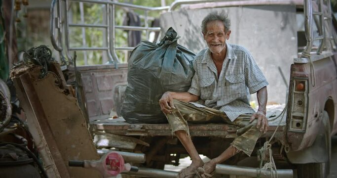 A smiling Asian man who is an elderly ragpicker or has a career collecting garbage and selling it, live in a slum village