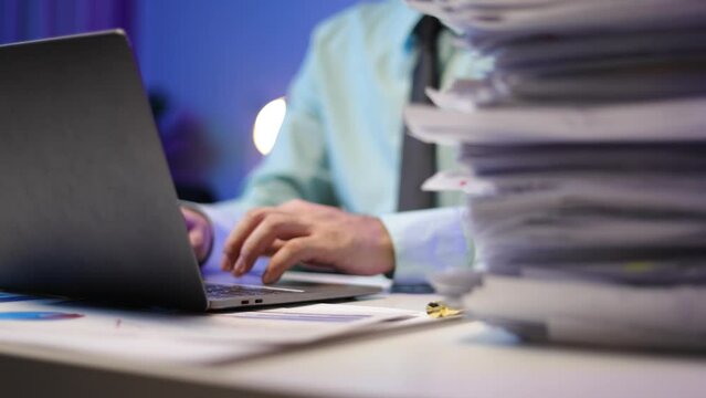 Man working with laptop and stack of documents on desk. Working to meet the deadline.
