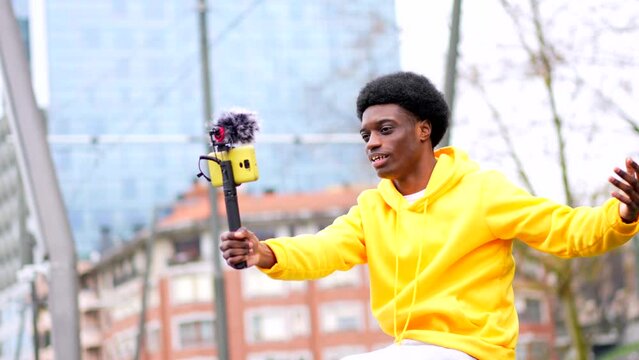 Side view video of a young african stylish vlogger recording video and waving in the city