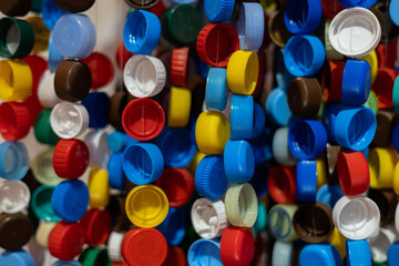 Multi-colored plastic caps hang in a row on a thread to form a beautiful backdrop. Waste plastic recycling. Composition of multi-colored plastic caps on a rope.