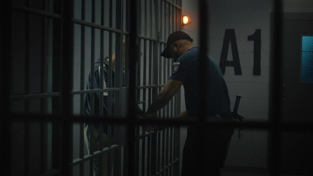 Warden takes off handcuffs from young prisoner. Teenager serves imprisonment term in correctional facility or detention center. Young inmate in prison cell. Justice system. View through metal bars.