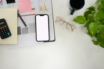 Top view smartphone with empty screen, glasses and business reports on white table
