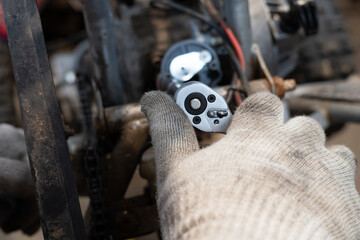 Close-up of a bolt being removed from a broken ATV part. A man holds a screwdriver in his hands and...