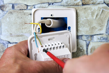 Connecting wires to wall thermostat for floor heating system, an electrician uses crosshead...