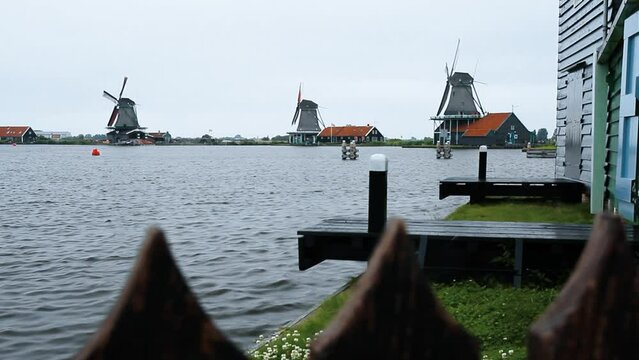 Movimiento de c&aacute;mara de derecha a izquierda. El r&iacute;o Zaan con el agua rizada provocada por el viento. Al fondo molinos de viento centenarios en funcionamiento en Zaanse Schans (Holanda)