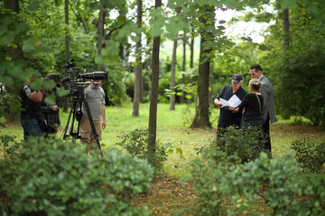 five man. one woman - Actors and assistents are standing in the park and shooting movie - obrazy, fototapety, plakaty