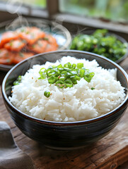 A dish of jasmine rice topped with green onions is placed on a wooden table, showcasing a simple...