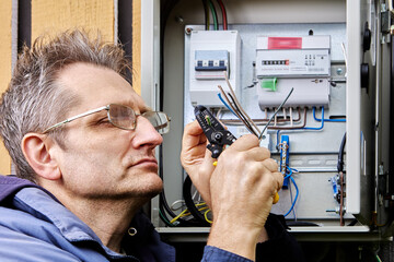 An electrician strips insulation from wire of three-phase power cable before connecting it to circuit breaker in an outdoor electrical panel.