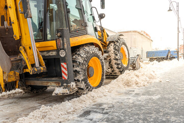 Cleaning city streets, a tractor-loader loads dirty snow into a dump truck. removal of snow and ice after heavy snowfalls and blizzards. Outdoor snow blower, sidewalk and driveway cleaning.