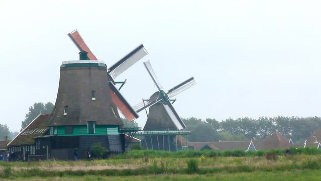 Paisaje holand&eacute;s de molinos de viento centenarios en funcionamiento con canales y gente paseando por camino circundante