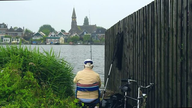 Plano cerrado de anciano pescando en el r&iacute;o Zaan. Al fondo la localidad de Zaandijk  