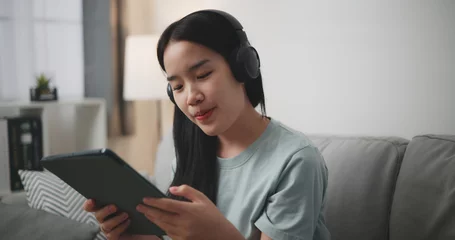 Papier Peint photo autocollant Magasin de musique Selective focus, Young asian woman wear wireless headphones sitting on sofa using digital tablet for online shopping cashless in living room at home