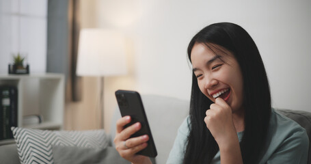 Selective focus, Happy young woman sitting on sofa looking at smartphone feel surprised while online shopping in living room at home - 759606537