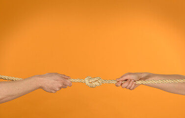 hands pulling a rope with a knot on an orange background