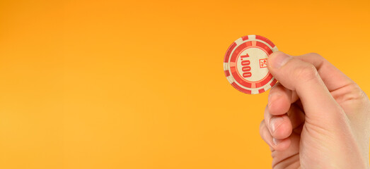 hand holding a poker chip on an orange background with free space for inscription text