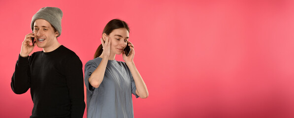 couple of satisfied joyful young people students talking using smartphones on a pink background with free space for text horizontal frame