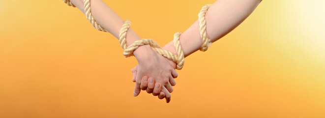a pair of hands holding each other tied with a rope on an orange background
