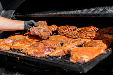 person grilling various cuts of meat on a barbecue. The meats are well-seasoned, and the grill has...