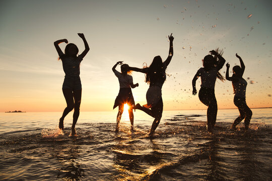 Silhouettes of happy girls are having fun and dancing at sunset lake beach