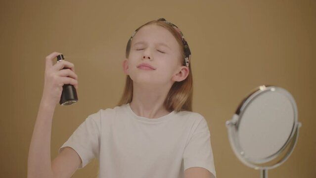 Pretty teenage girl spraying facial spray or soothing moisturizing toner. Spraying process, water droplets flying in slow motion. Concept beauty and skincare products for teens.