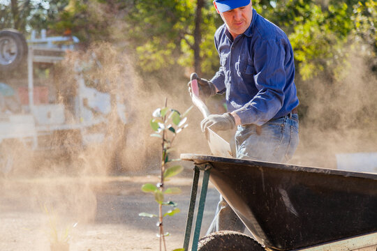 Man shoveling dry dusty dirt into a wheelbarrow, gardening
