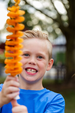Smiling boy holding up hot chips on a stick &ndash; tornado potatoes