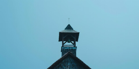 Old Retro Bell Tower Against Blue Sky background with copy space. Orthodox bell tower of a traditional church with cross on top. Bell ringing, the work of the bell ringer.
