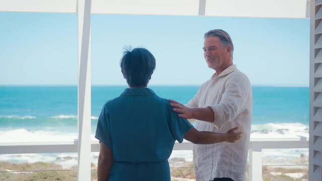 Loving mature couple on holiday in beach front property overlooking ocean hugging - shot in slow motion