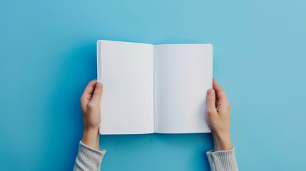 Female hands holding an opened blank notebook mockup, shot from the top, isolated blue background...