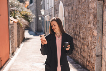 Beautiful smiling woman walking on street with coffee takeaway to go, chatting on mobile phone....