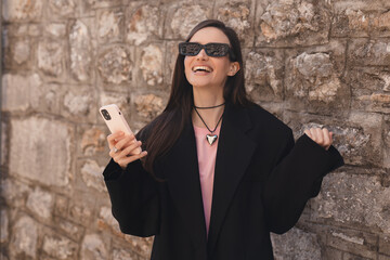 Happy smiling young brunette woman hold smartphone with excited face expression, unable to believe that she bet played, win in lottery, read good news, can't believe in her fortune. Girl wear glasses.