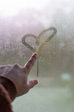 Finger drawing heart in condensation on winter window
