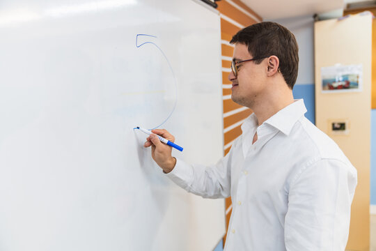 Pensive man with Down Syndrome writing numbers on board. - Powered by Adobe