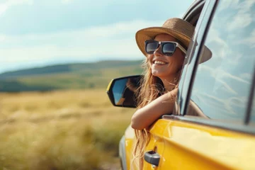 Poster Happy woman enjoying a car journey on a summer road trip, happy young smiling girl wearing sunglasses and a hat sitting on the car window open leaning out from the car door looking at the landscape  © inthasone