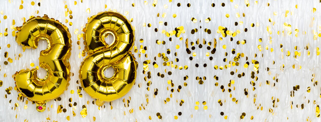 Golden foil balloon number, figure thirty-eight on white with confetti background. 38th birthday...