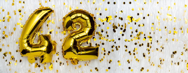 Golden foil balloon number, figure forty-two on white with confetti background. 42th birthday card....