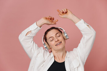 Modern woman smiling with braces on her teeth and listening to music in headphones and dance on pink background