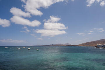 Seascape, calm sea. Group of boats anchored nearby. Mountains in the background. Turquoise Atlantic Ocean. Big white clouds. Village of Arrieta. Lanzarote, Canary Islands, Spain